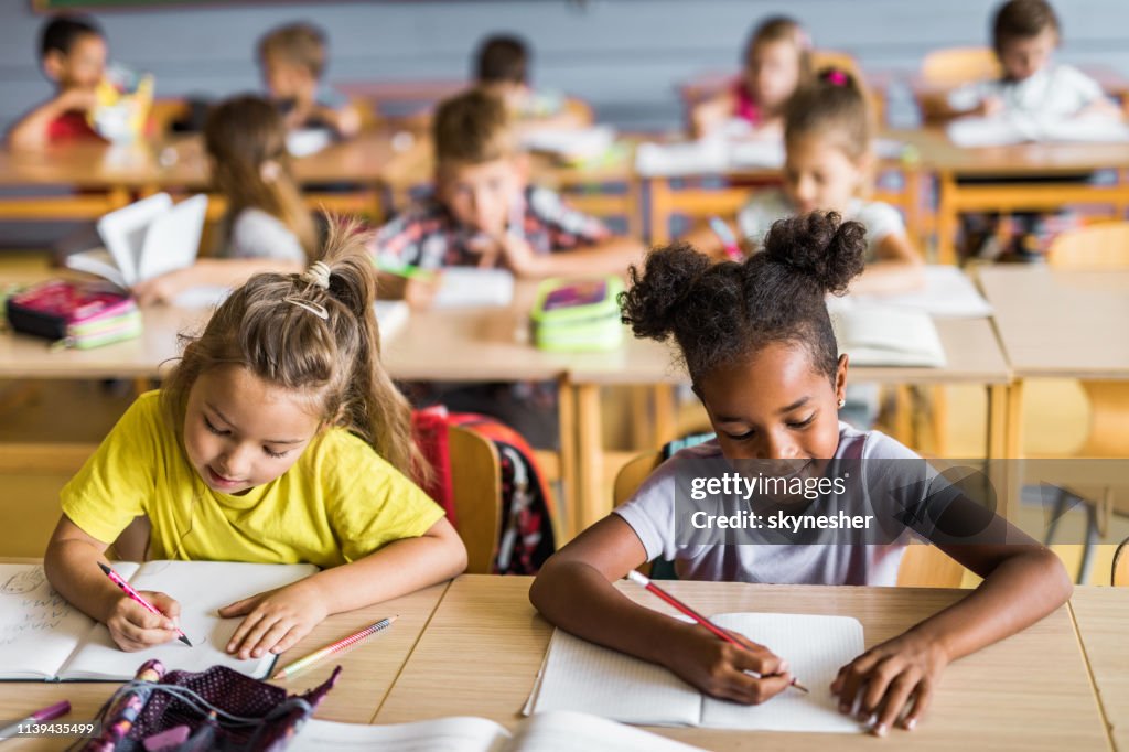 Happy schoolmeisjes het schrijven van een dictee op een klas op school.