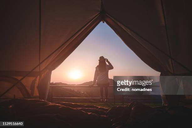 Woman traveler sitting outside camping tent and looking at sunrise view and mountain range.Travel outdoors camping for exploration and freedom concept.