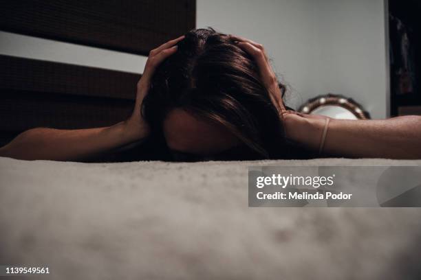 young woman lying on bed face down with ears covered - domestic violence stock pictures, royalty-free photos & images