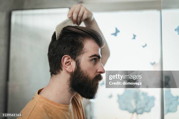 young man combing hair in the bathroom - beard care stock pictures, royalty-free photos & images