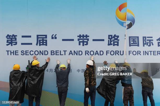 Workers take down a Belt and Road Forum panel outside the venue of the forum in Beijing on April 27, 2019. - Chinese President Xi Jinping urged...