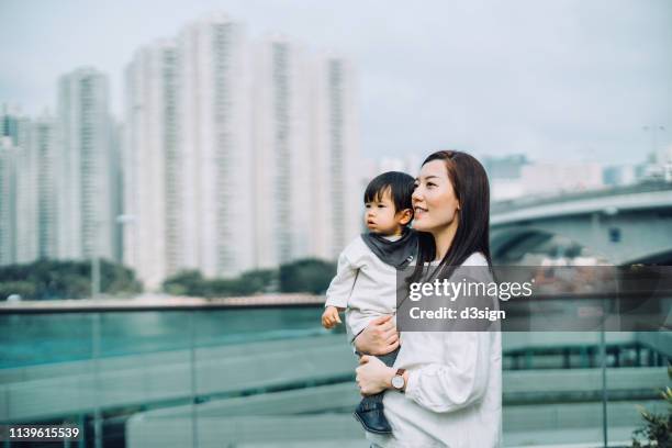 young asian mother carrying daughter standing on urban balcony overlooking city view against urban cityscape - looking over balcony stock pictures, royalty-free photos & images