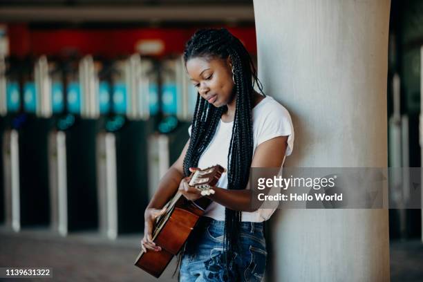 beautiful braided hair young woman playing guitar whilst leaning against a pillar - plait stock-fotos und bilder