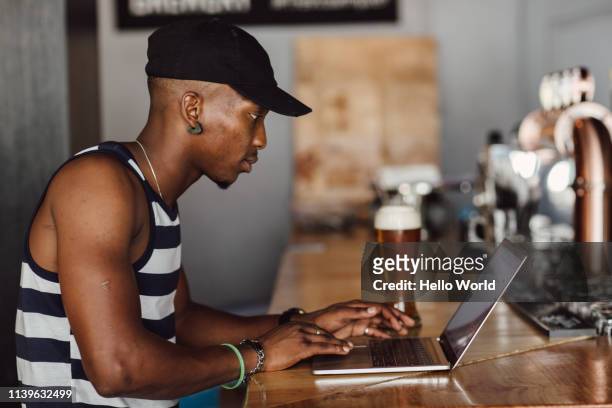 Side view of casually dressed young man working with laptop on a bar countertop