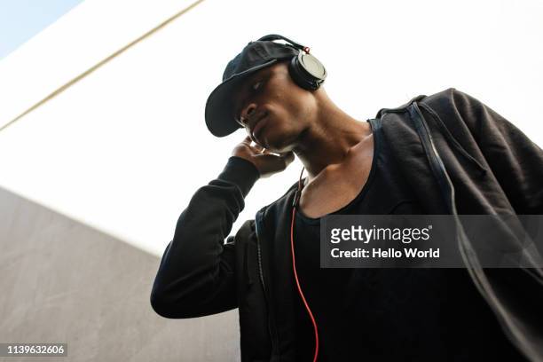 low angle view of young man wearing black listening to music with earphones - headphone man on neck stockfoto's en -beelden