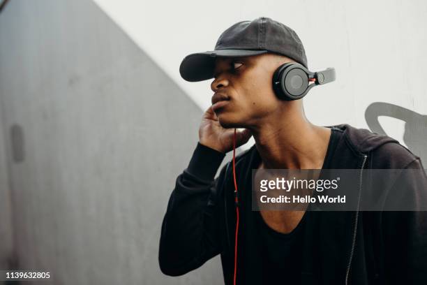 Side view of handsome young man wearing black listening to music with earphones