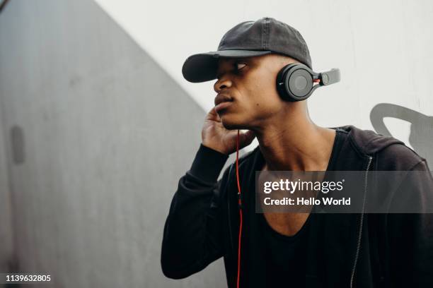 Side view of handsome young man wearing black listening to music with earphones