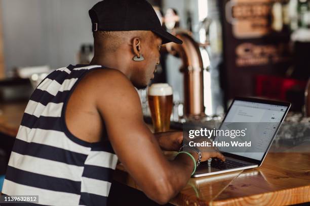 rear side view of casually dressed young man working with laptop on a bar countertop - world café stock pictures, royalty-free photos & images