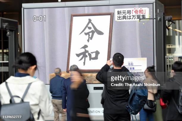 People walk past a big screen displaying the news after the new imperial era name 'Reiwa' is announced on April 01, 2019 in Osaka, Japan. The new era...