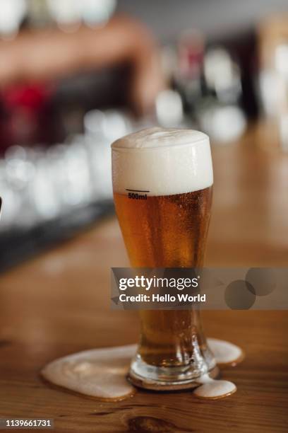 overflowing pint of beer on a wooden counter table top - natale stockfoto's en -beelden