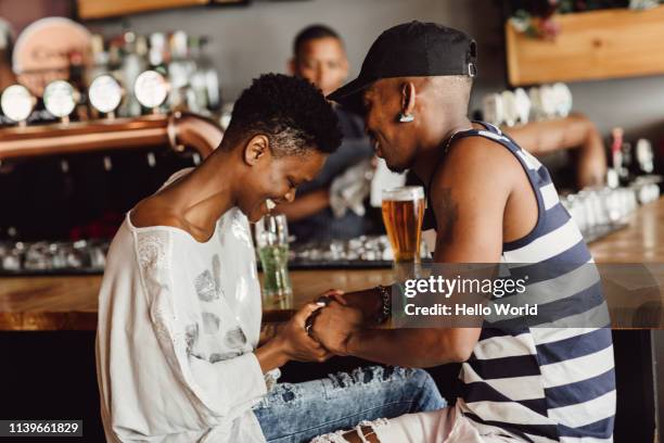 beautiful smiling and affectionate couple holding hands whilst seated at bar drinking beer. - atividade romântica - fotografias e filmes do acervo
