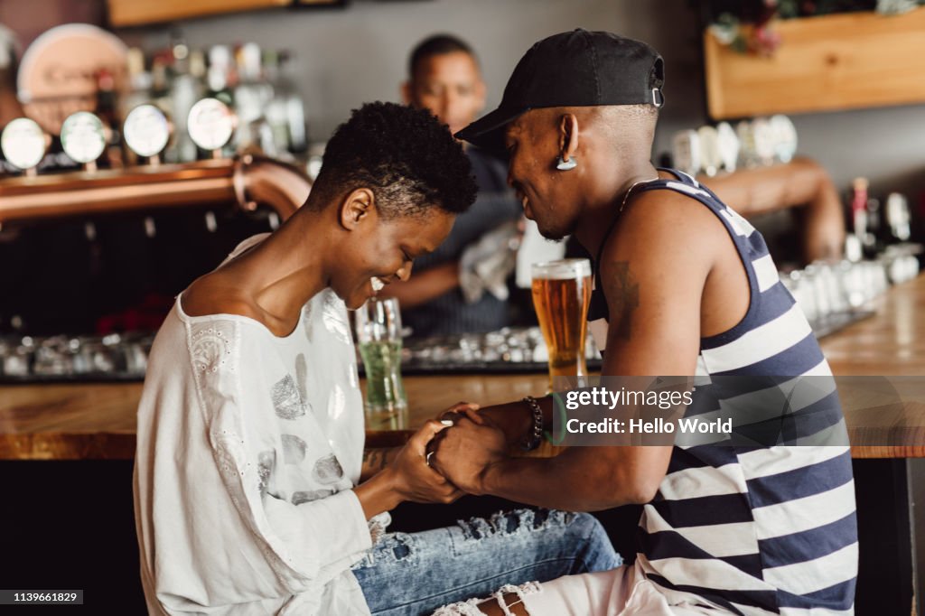 Beautiful smiling and affectionate couple holding hands whilst seated at bar drinking beer.