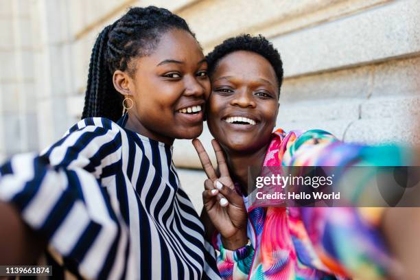 beautiful happy girlfriends taking a selfie whilst showing victory sign with hands - femmes africaines photos et images de collection