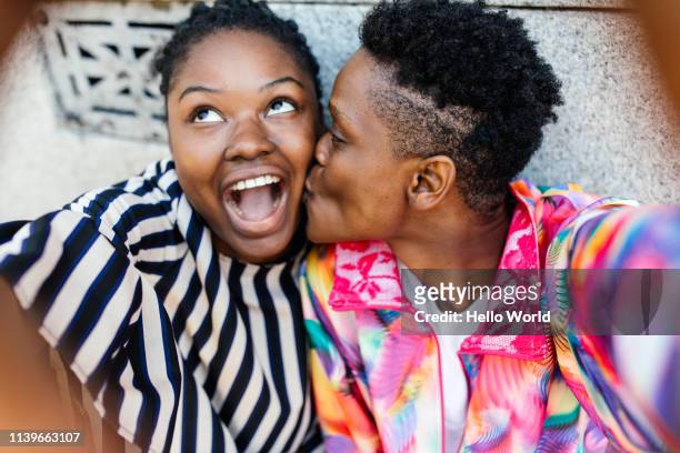 Beautiful happy girlfriends taking a kissing on the cheek selfie with mobile phone