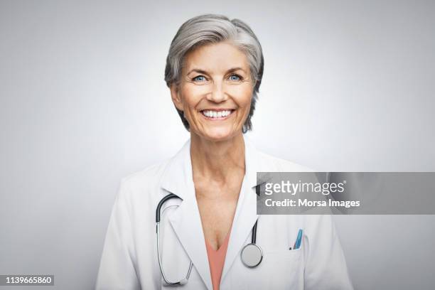 senior female doctor smiling on white background - doctor portrait stock-fotos und bilder