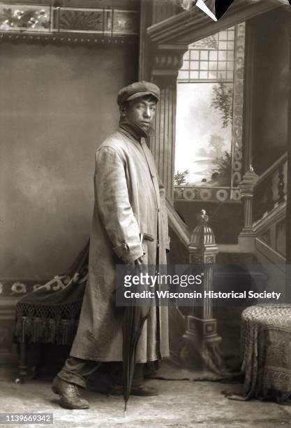 Full-length studio portrait of a Ho-Chunk man, Will Goodvillage , posing standing in front of a painted backdrop near a chair, Black River Falls,...