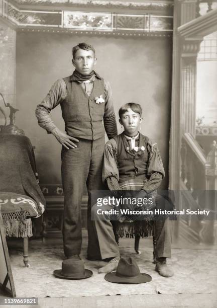 Full-length studio portrait of two young Ho-Chunk men posing in front of a painted backdrop, Black River Falls, Wisconsin, 1900. The man on the right...