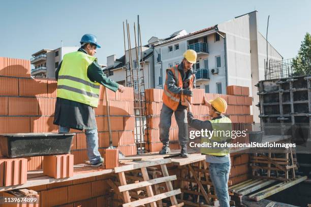 bauarbeiter bauen am dach des gebäudes eine ziegelmauer - bauarbeiter stock-fotos und bilder