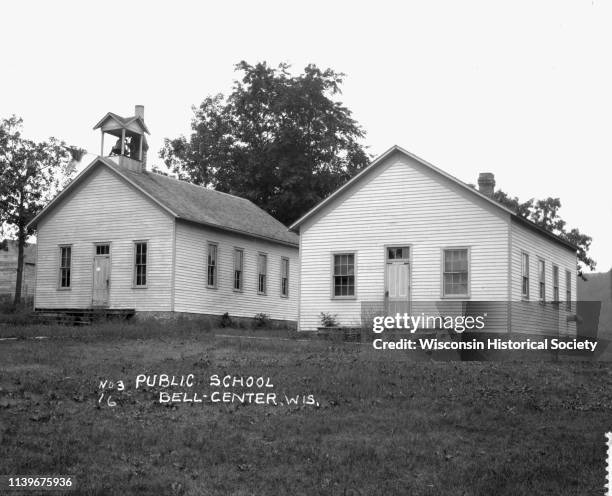 Exterior view of two public school buildings, Bell Center, Wisconsin, 1916. The left building has a bell tower, with a flag hanging horizontally from...