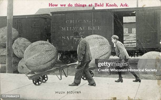 Man and a boy use dollies to haul giant musk melons near a train, Waupun, Wisconsin, 1911. In red text on the upper center portion is the...