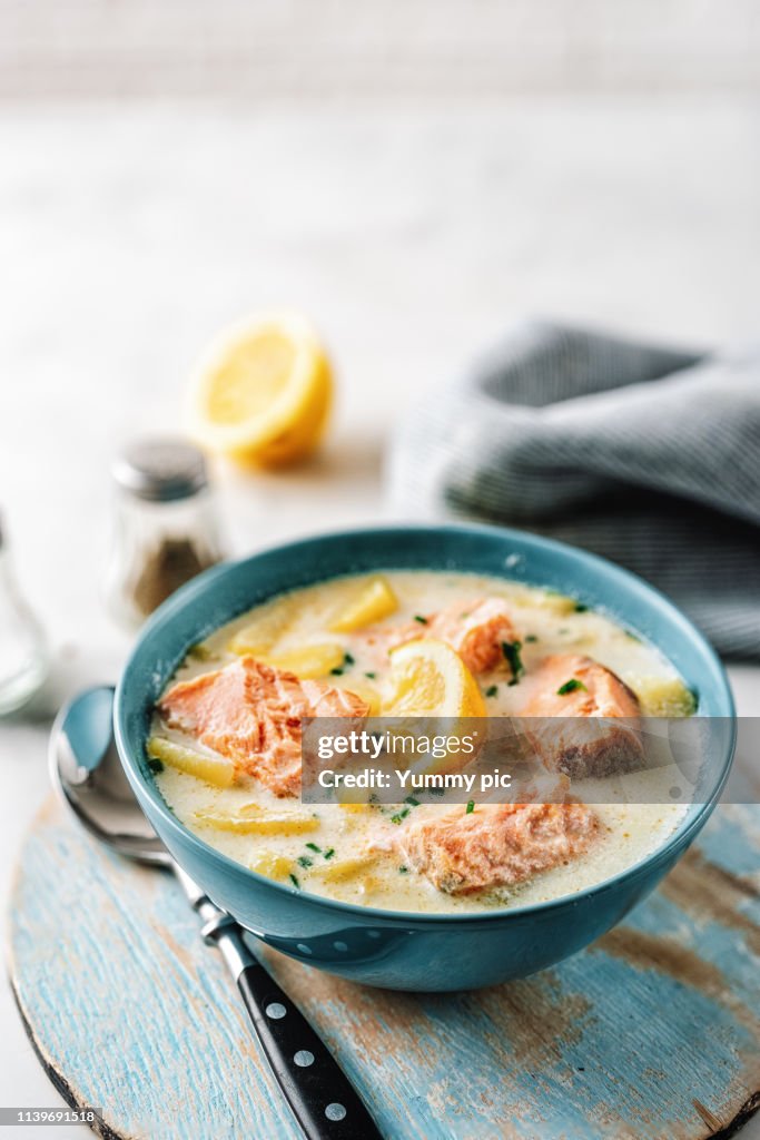 Soup with salmon and potatoes in a blue bowl on bright wooden tray
