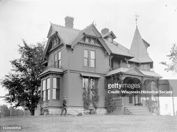 Boy mowing the lawn in front of an elaborate Victorian frame house, probably the residence of WR O'Hearn located at Tenth and Harrison Streets, Black...
