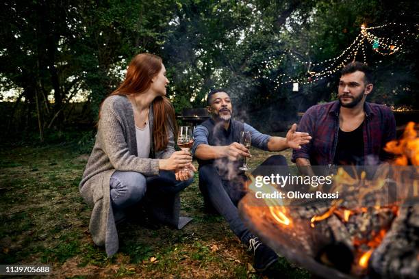 three people sitting at campfire on a garden party - garden party stock-fotos und bilder