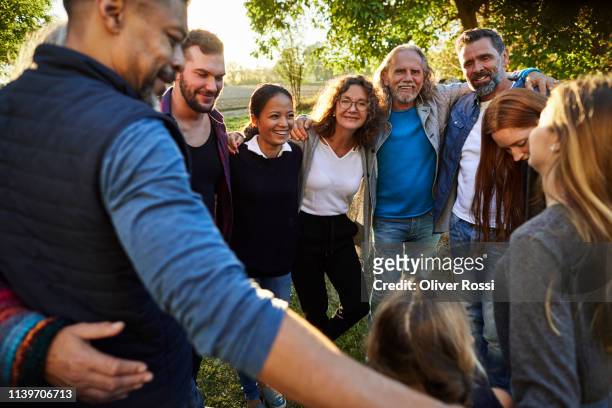 group of happy people embracing on a garden party at sunset - zusammenhalt stock-fotos und bilder
