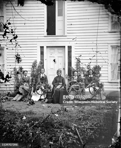 Siri Rustebakke, center, sits in front of a house with her daughters and daughter-in-law and four spinning wheels, Black Earth, Wisconsin, 1873....