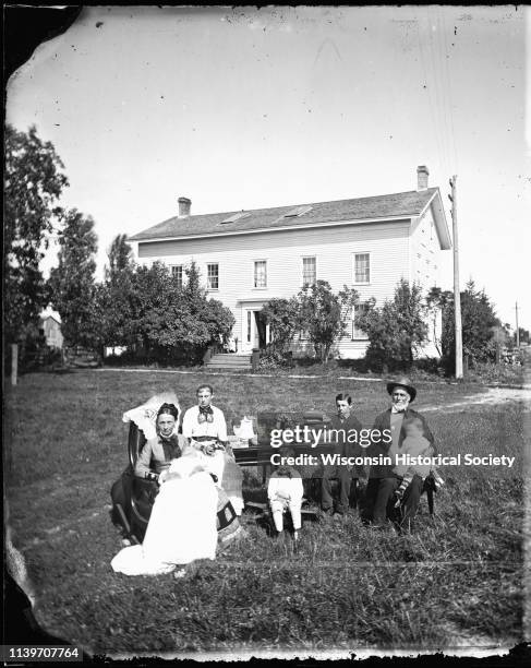 The William McFarland family is gathered around a table covered with books, pine cones, glassware and flowers in front of their Exchange Street house...