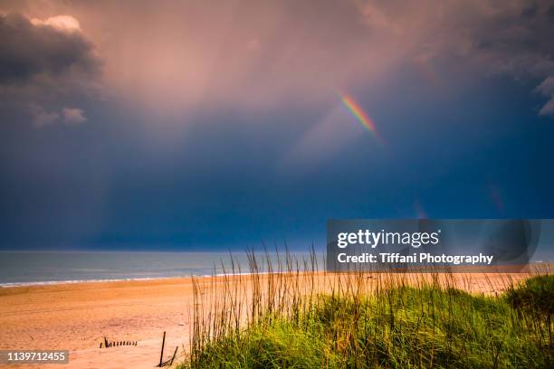 partial rainbow over partial beach dunes with grass and clouds showing - horizontal orientation - outer banks stock pictures, royalty-free photos & images