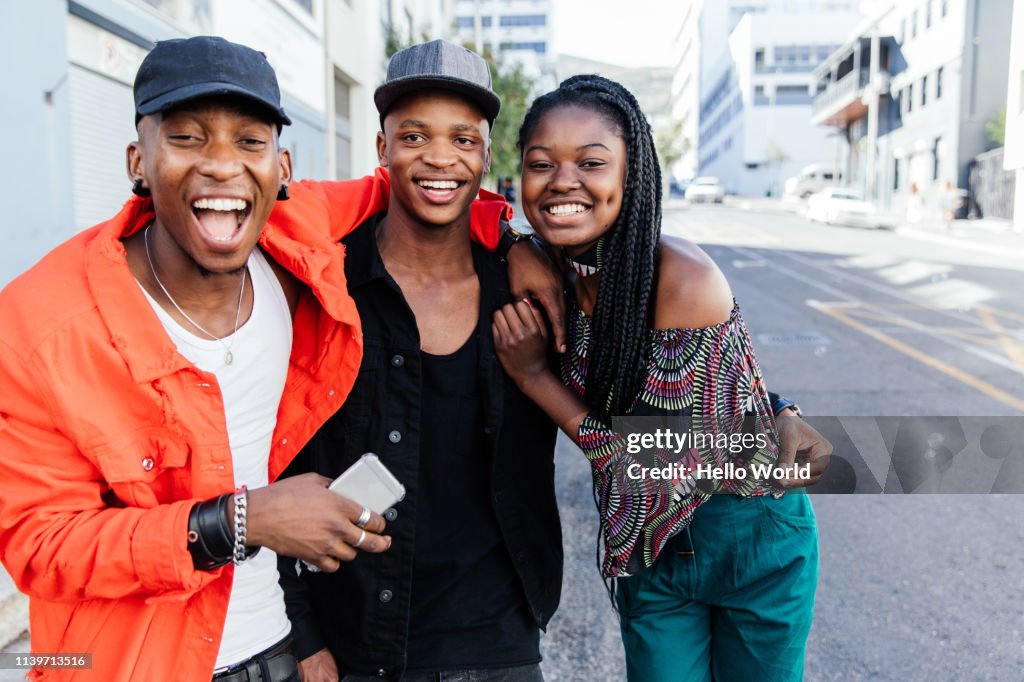 Three beautiful happy embracing friends laughinginto camera on city street