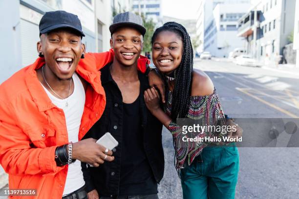 three beautiful happy embracing friends laughinginto camera on city street - south africa stock pictures, royalty-free photos & images