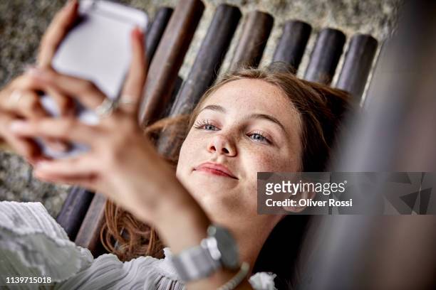 smiling young woman lying on a bench using cell phone - man on bench stock-fotos und bilder