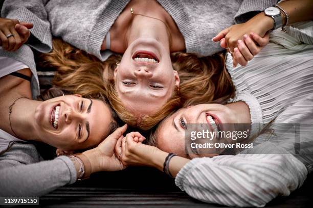 three happy young women lying on a bench holding hands - tres amigos fotografías e imágenes de stock