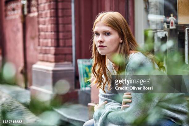 serious young woman sitting at house entrance - introspektion stock-fotos und bilder