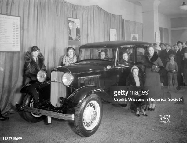 Six Lido Ladies, an act performing at the Orpheum Theatre, posing with a new Ford V8 car in the lobby of the Orpheum Theatre with a crowd looking on,...