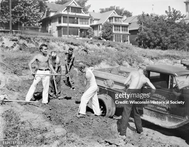 Five University of Wisconsin-Madison athletes shoveling dirt at Camp Randall with a Fay Hammersley Jr Excavating truck parked nearby, Madison,...