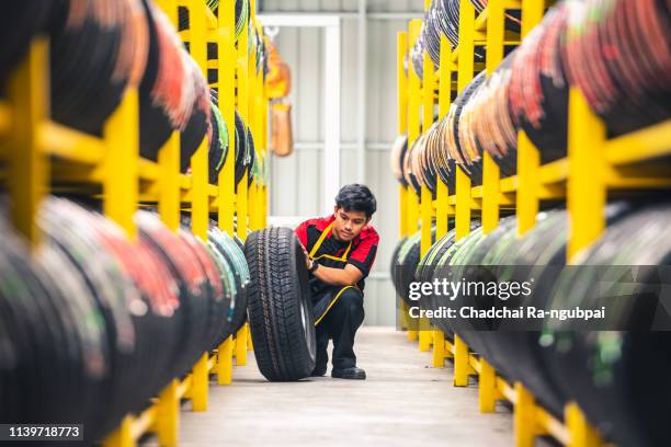 mechanic pulls tire from the tyre store warehouse - pezzo di ricambio foto e immagini stock