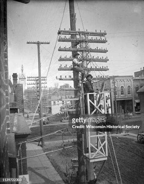 Elevated view of men working on telephone lines from scaffolding attached to the pole in front of the telephone exchange building, Black River Falls,...