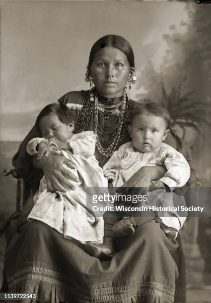 Studio portrait of Mountain Wolf Woman, also known as Stella Blowsnake Whitepine Stacy , sitting and holding her two daughters, Josephine Whitepine...