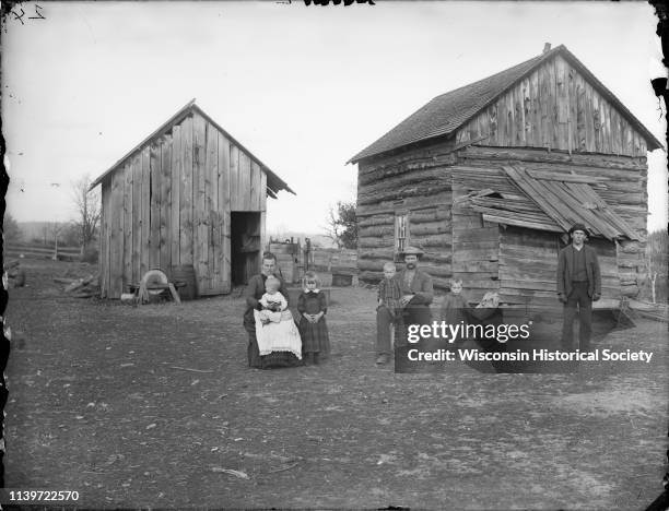 Man and woman posing sitting, each holding a child in their lap, and a young man, girl, and a boy holding a toy horn, are posing standing, Black...