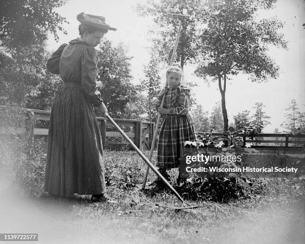 Woman in hat and young girl raking the lawn, Black River Falls, Wisconsin, 1910.