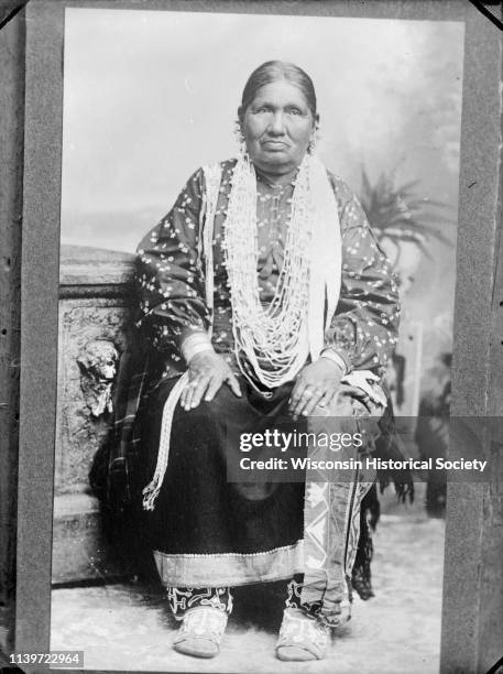 Betsy Thunder, Ho-Chunk medicine woman, posing in front of a painted backdrop near a prop stone wall, Black River Falls, Wisconsin, February 6, 1913.