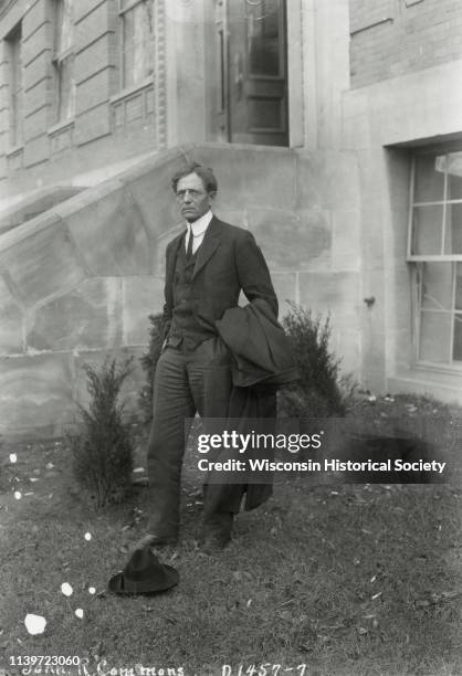 John R Commons, a University of Wisconsin professor, is shown standing outside Sterling Hall with his hat on the ground at his feet, Madison,...