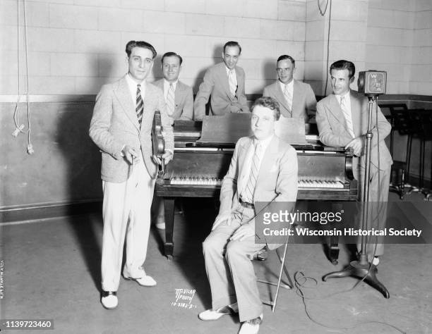 Anthony 'Tony' Salerno's Gypsy Melodians at WIBA radio station standing around a piano, Madison, Wisconsin, August 23, 1932. Tony is holding his...