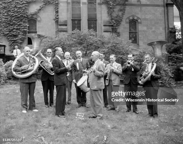 Reunion of eight members of the 1915 University of Wisconsin world's fair band with their instruments, director Charles Mann, and current UW Band...