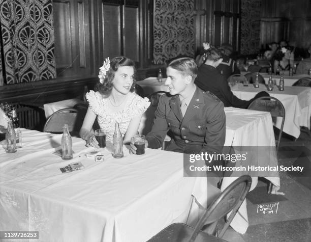 Formally dressed young woman and her beau in his US Army uniform sit at a table and drink Coca-Cola at the 'Moonlight Formal' in Tripp Commons at the...