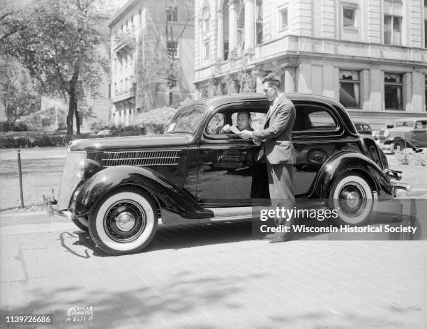 Salesman standing beside new Ford car, parked beside the UW YMCA, 740 Langdon Street, with Harry Stuhldreher, University of Wisconsin-Madison...