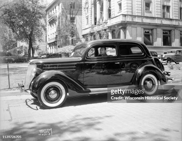 Harry Stuhldreher, University of Wisconsin-Madison head football coach, sitting in new Ford car in front of UW YMCA building, 740 Langdon Street,...